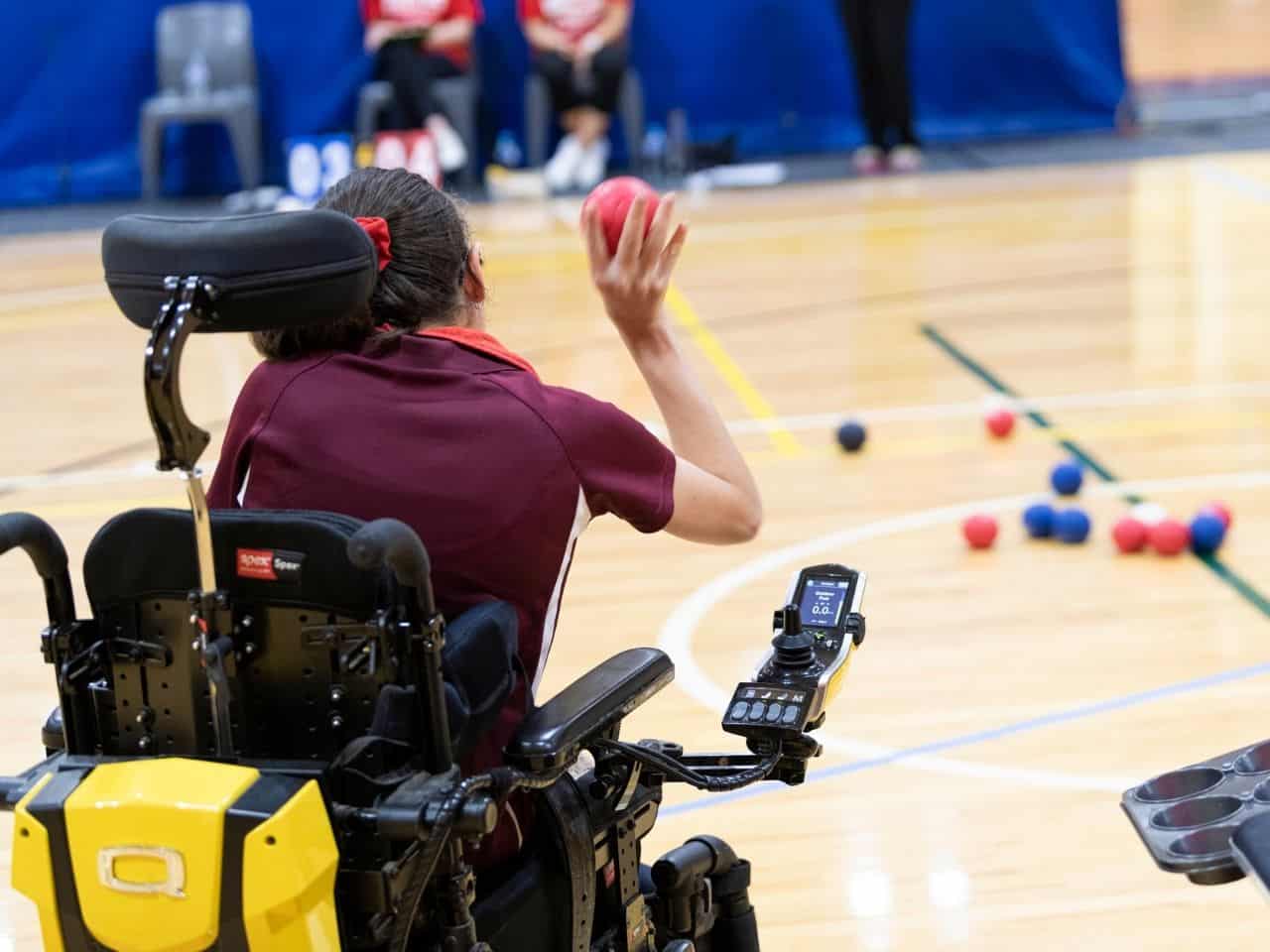 A female athlete sitting in her wheelchair throws a ball during a game of Boccia.