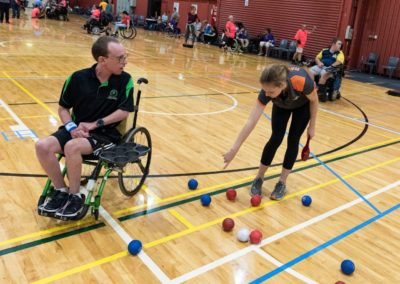 A referee and boccia player discuss the ongoing game of boccia being played.