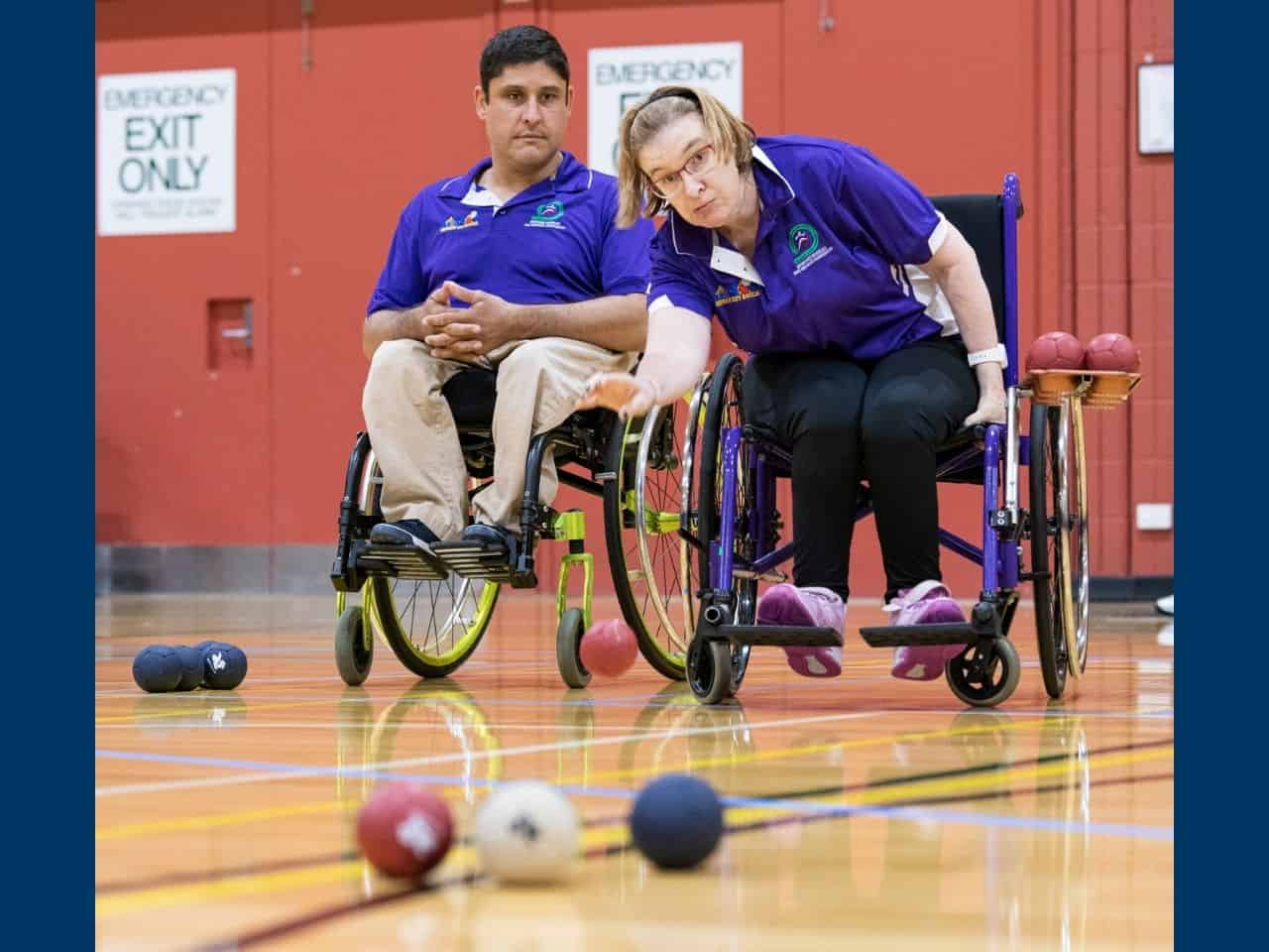 A female boccia players rolls the ball during a game as another player watches on.