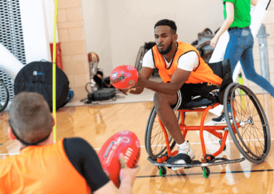 Male amputee demonstrates how to play wheelchair AFL to children.