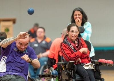 An athlete mid-throw while onlookers cheer during a game of boccia.
