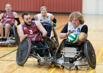 One wheelchair rugby player chases another player down the court in a competitive match.
