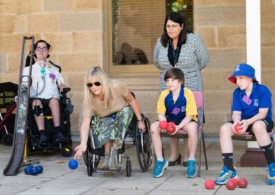 A female wheelchair user demonstrates to school students how to place boccia from the chair at a Sporting Wheelies school visit.