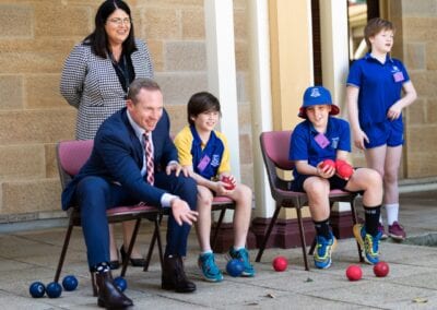 School teacher joins in with the students as they play boccia while sitting in chairs.