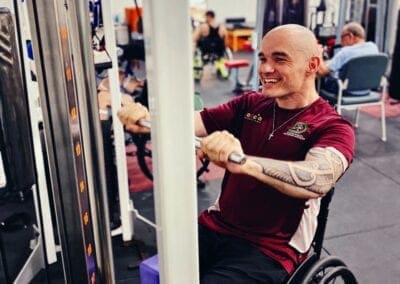 Male client uses weights while in his wheelchair as a part of the gym and group fitness program at Sporting Wheelies.