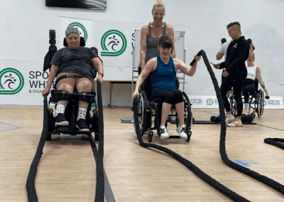 Female clients in wheelchairsdoing battle ropes in a Sporting Wheelies group fitness class.