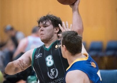 Male wheelchair basketball player tries to pass the ball while being defended.