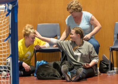 Two female teammates sit next to each other while watching a game of goalball.