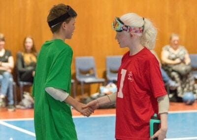 Two opposing Goalball athletes shake hands with each other.