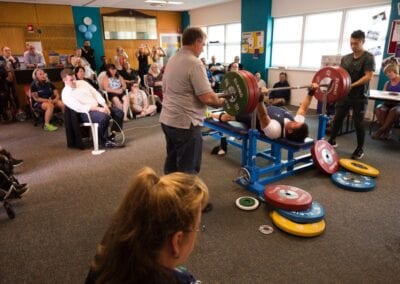 Spectators watch as a para athlete attempts to lift weights in a power lifting competition.